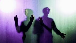 Photo of two shadowy figures behind a purple and green curtain