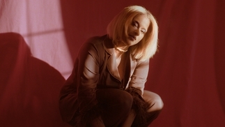 Photo of L’Rain crouching in a red dress in front of a shadowy red background