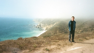 Photo of Anthony Naples standing near a grassy cliff, a bright blue sea is in the background