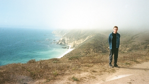 Photo of Anthony Naples standing near a grassy cliff, a bright blue sea is in the background