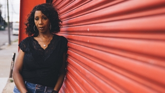 DJ Minx poses next to a red-painted garage door