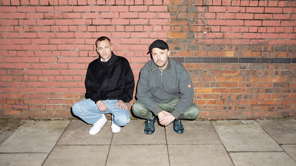 The Overmono brothers crouched in front of a red brick wall