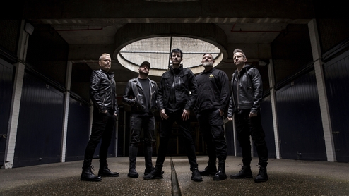 Photo of the five members of Pendulum standing in an industrial space.