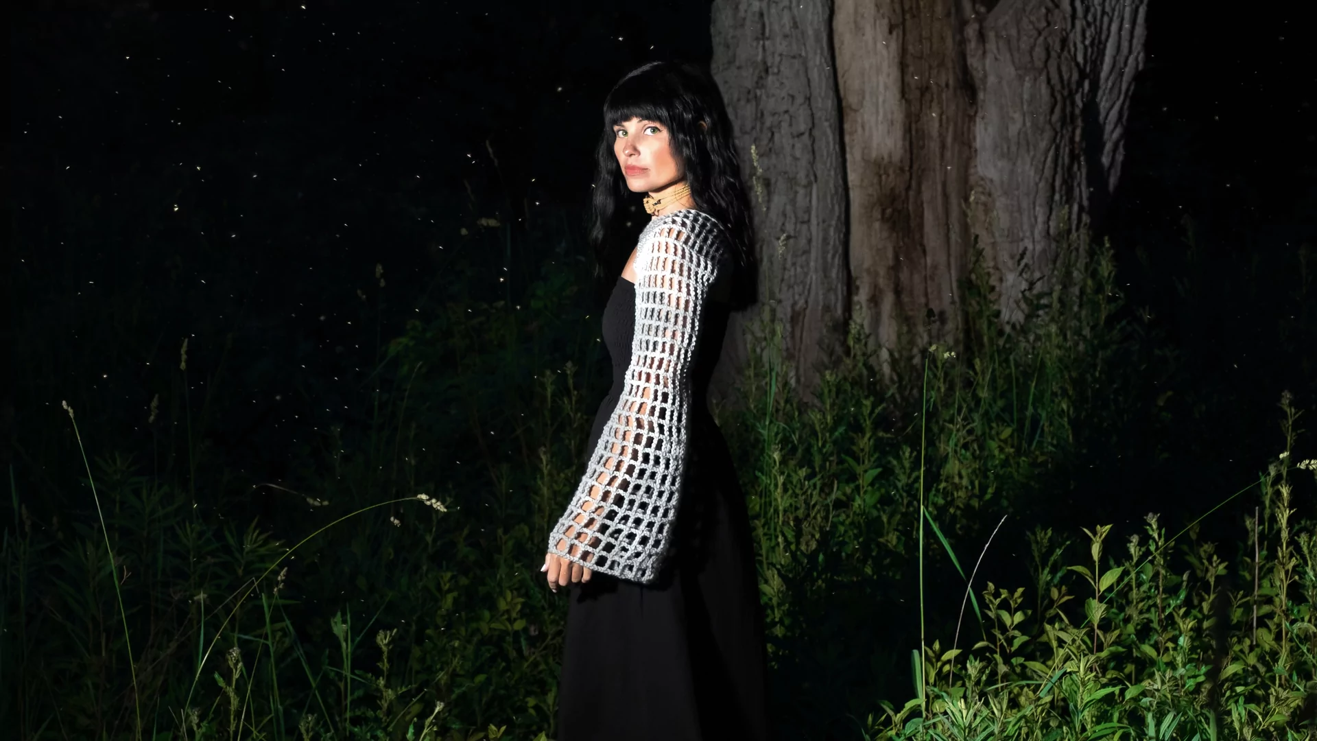Photo of Born Days wearing a black dress and mesh shawl standing in front of a large tree
