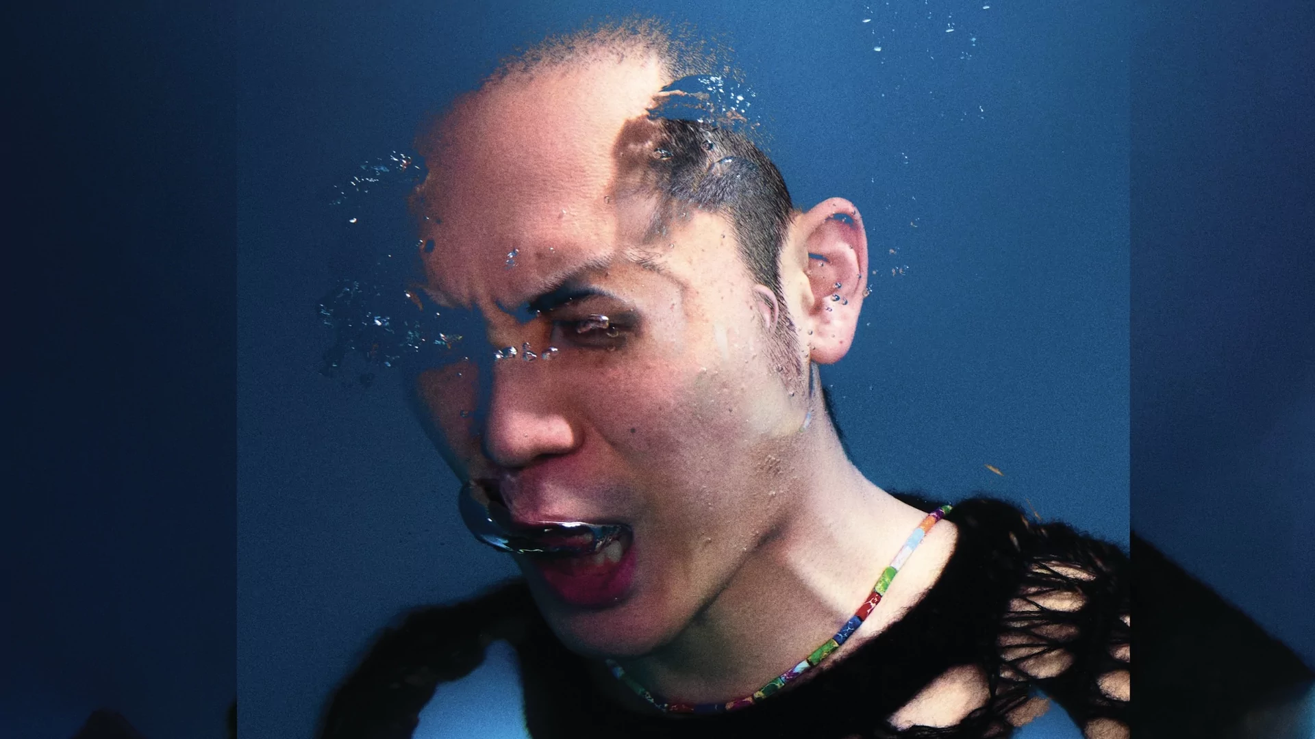 Photo of Tzusing wearing a black distressed jumper while breathing out bubbles underwater